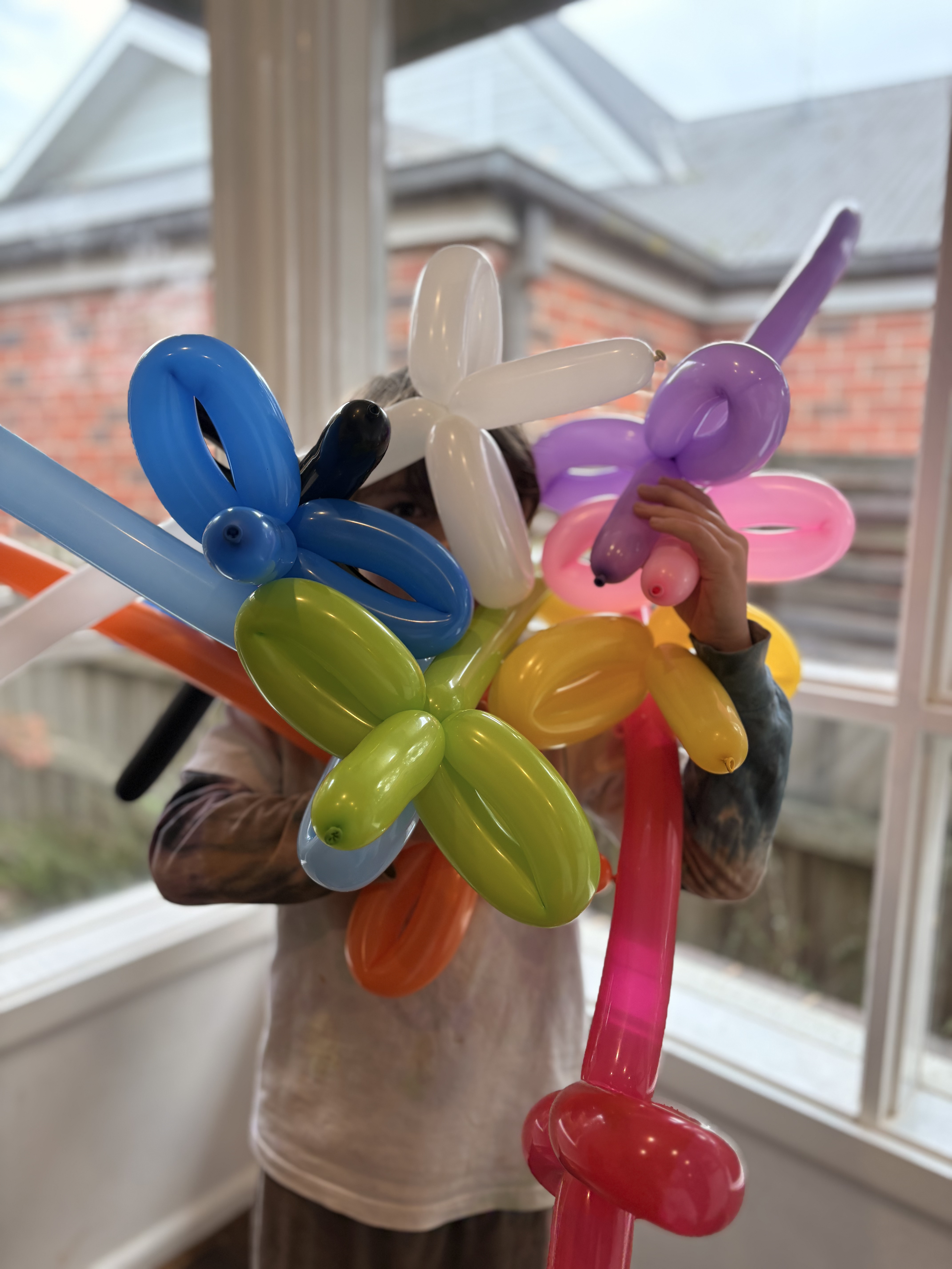 A child holding a rainbow armful of twisted balloon swords, dogs and flowers